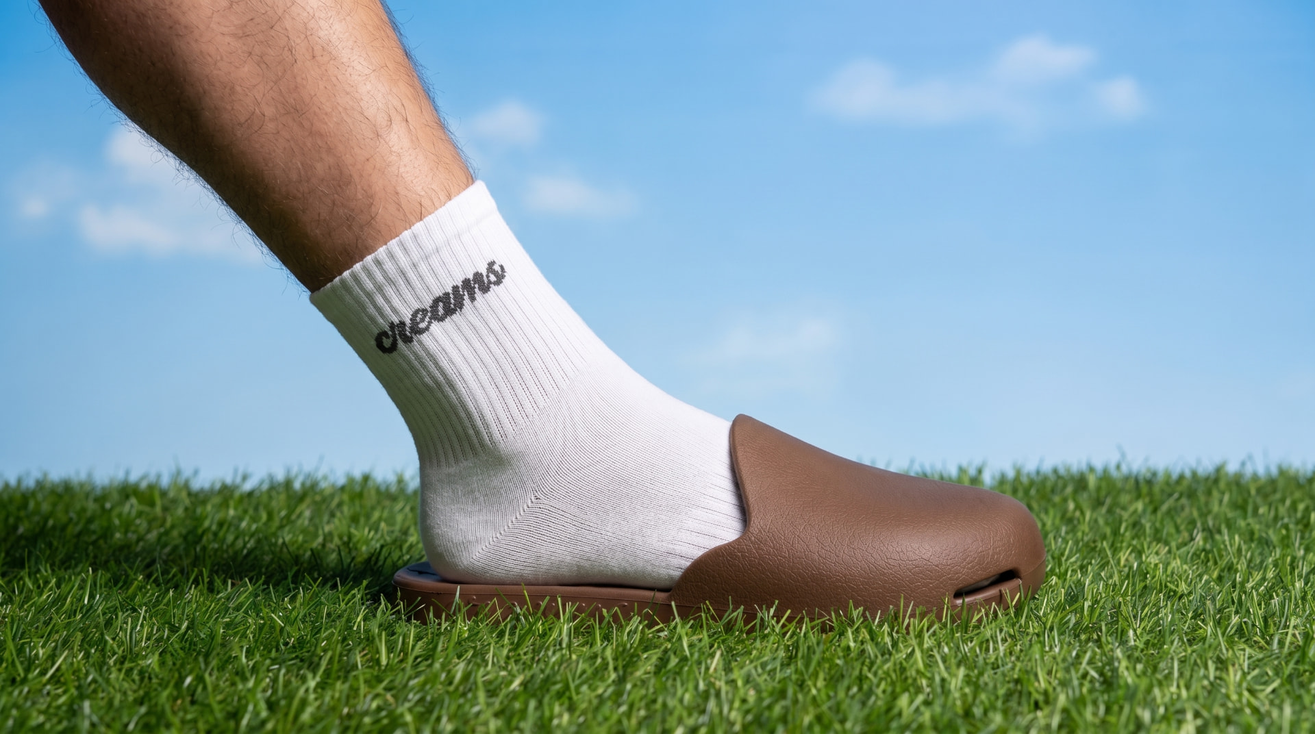 Creams ribbed crew sock in white with script logo, worn with a brown slide on grass